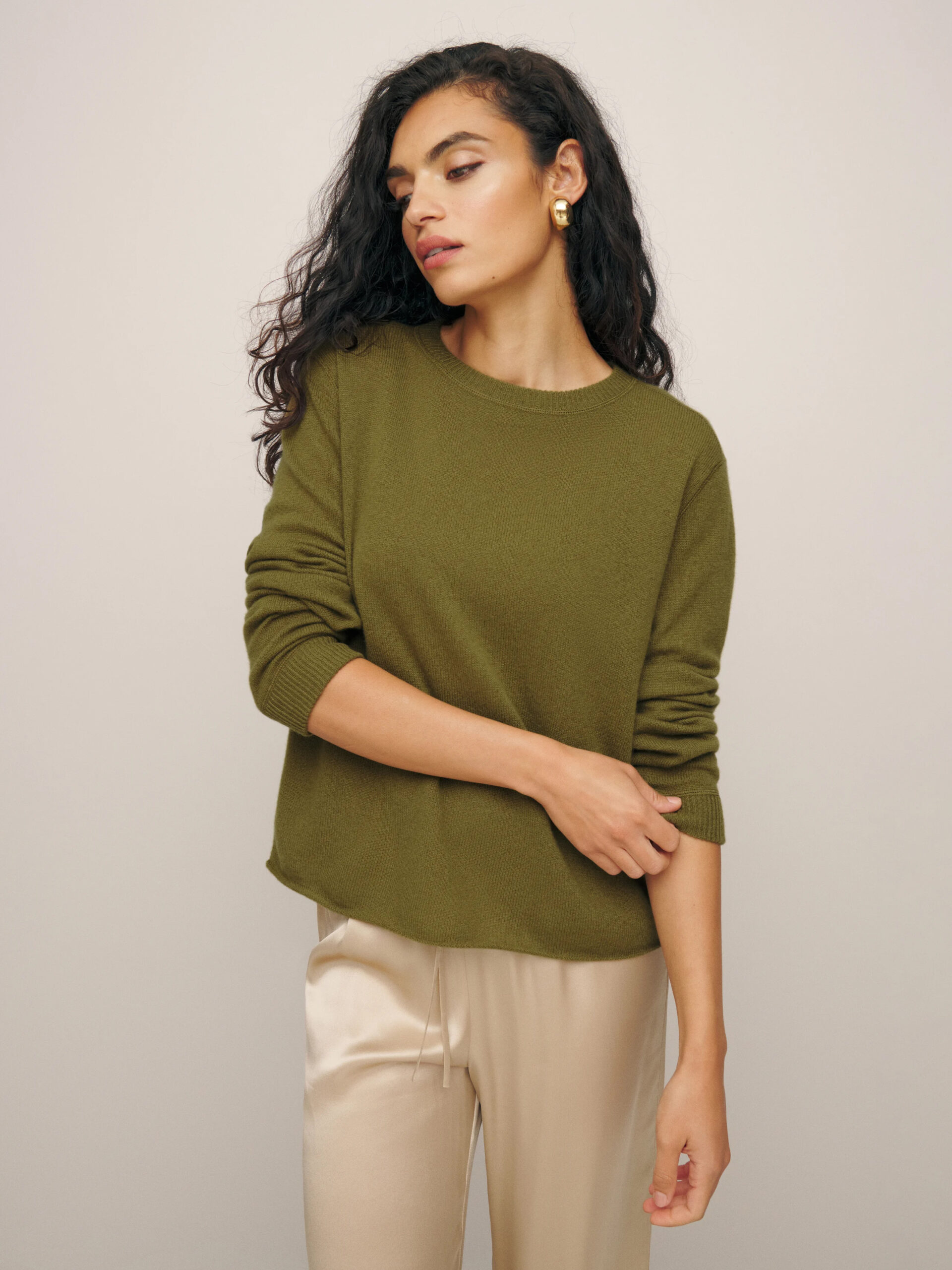 A woman in a green sweater and beige pants posing with her hand on her hip.
