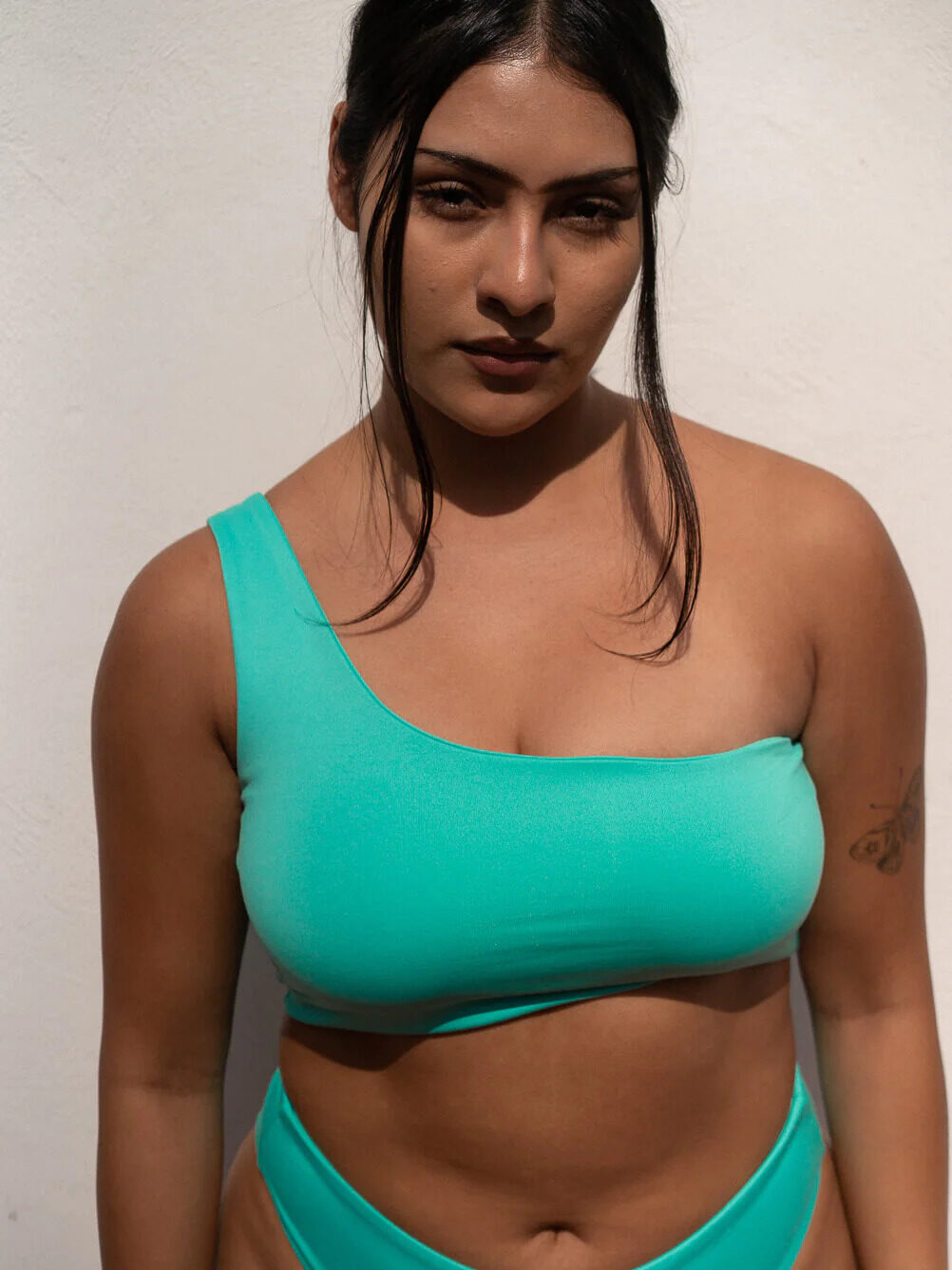 Woman in turquoise sportswear standing against a white wall.