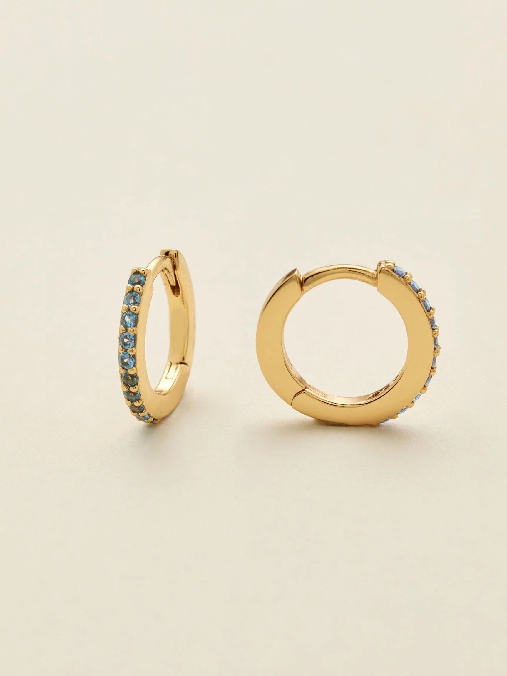 A pair of gold hoop earrings with blue gemstone accents on a light background.