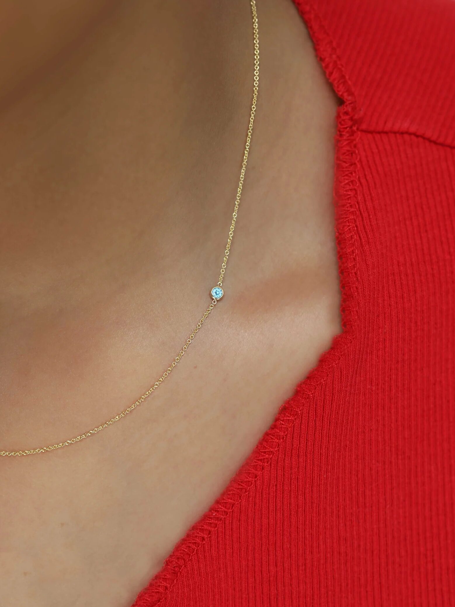 Close-up of a person wearing a gold chain necklace with a small pendant against a red top.