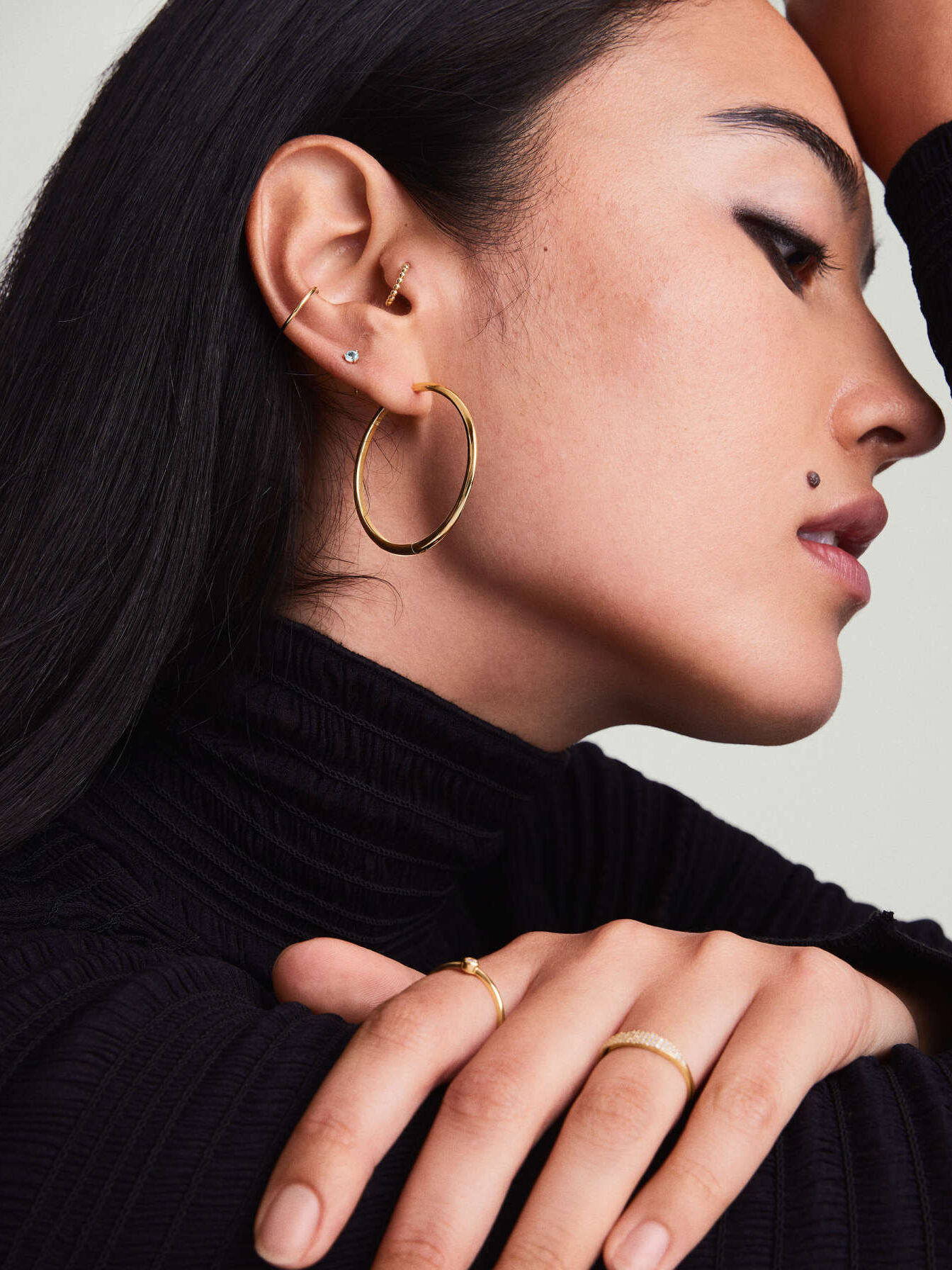 Profile of a woman wearing hoop earrings and rings, with a black turtleneck sweater.