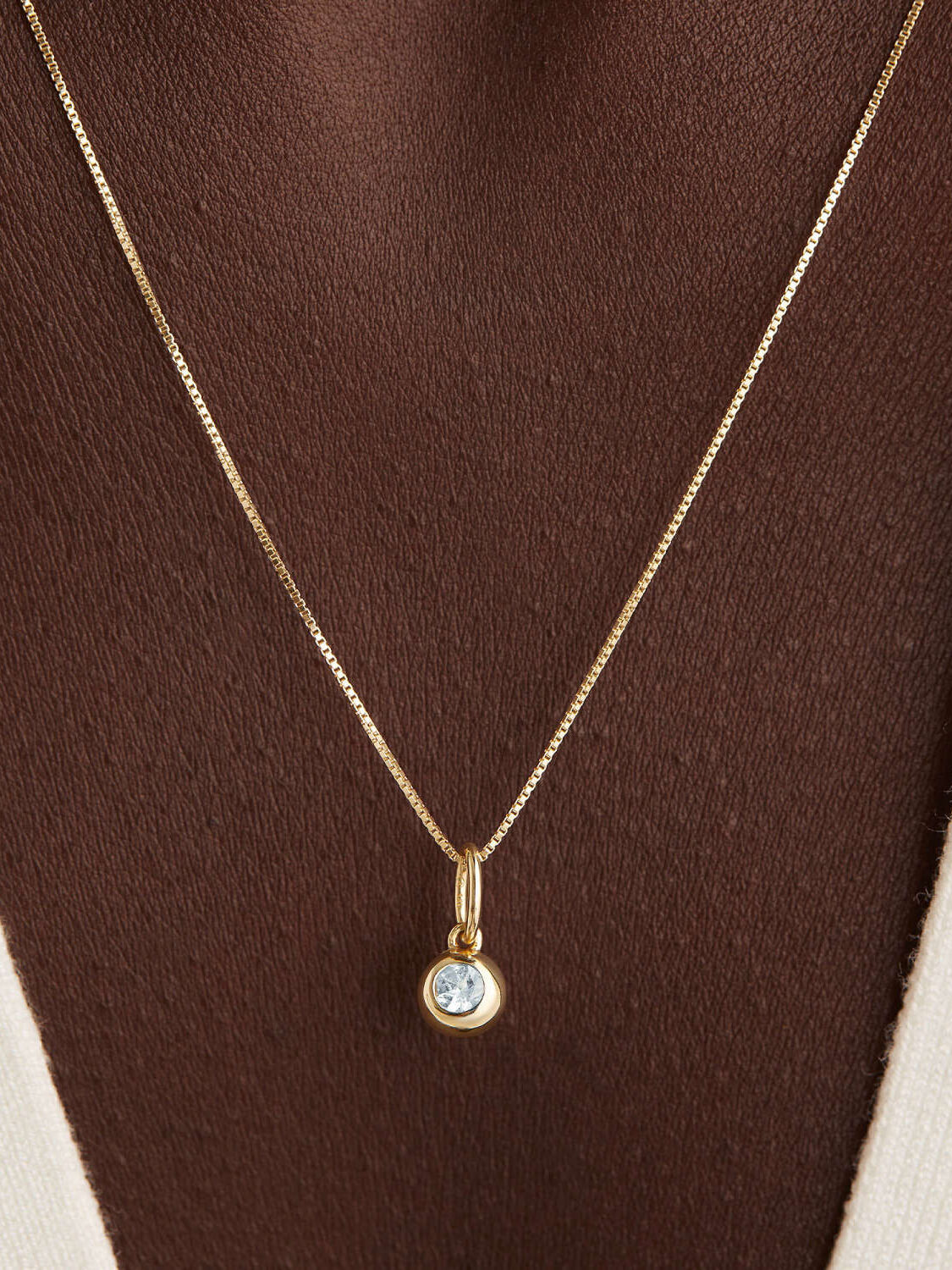 Gold necklace with a single pendant on a person wearing a white top.