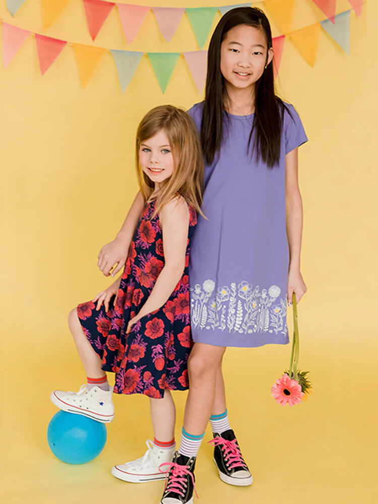 Two girls in purple dresses posing in front of a yellow background.