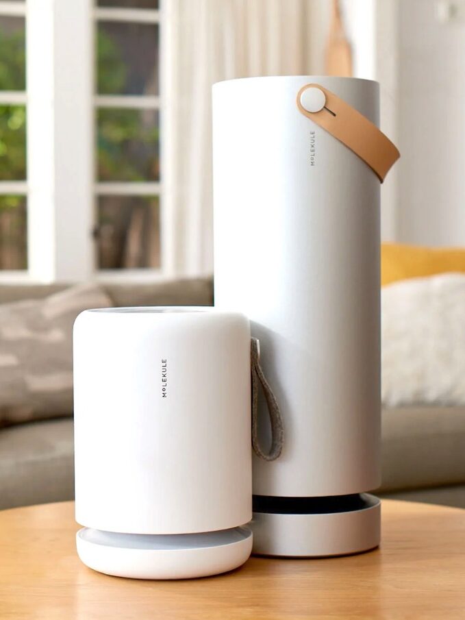 Two modern portable air purifiers of different sizes on a wooden table in a living room setting.