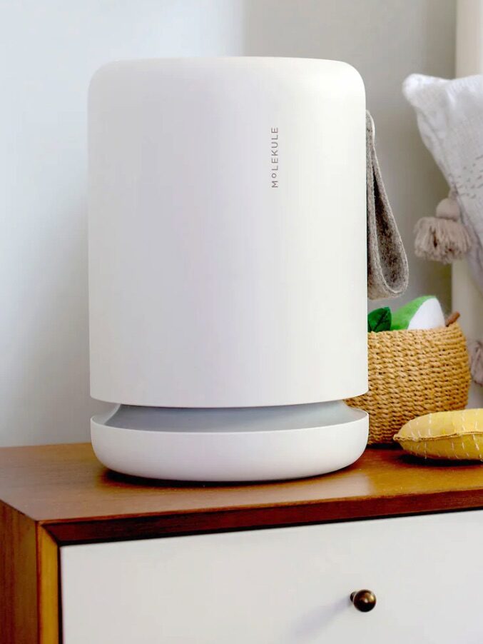 A white portable air purifier placed on a wooden nightstand in a bedroom setting.