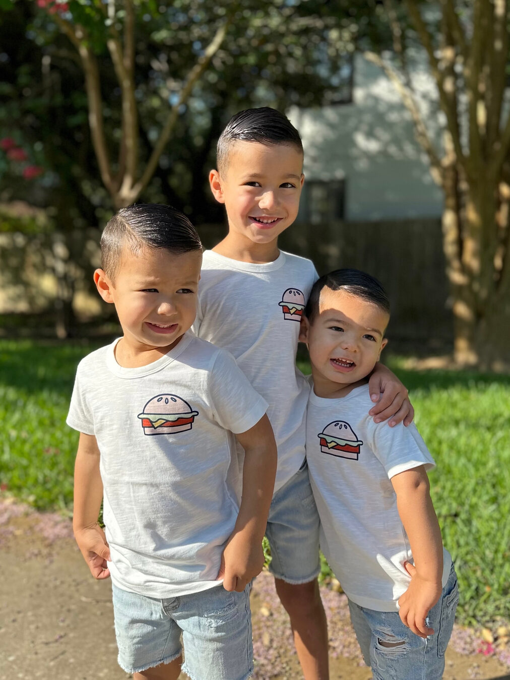 Three young boys posing for a picture in front of a tree.