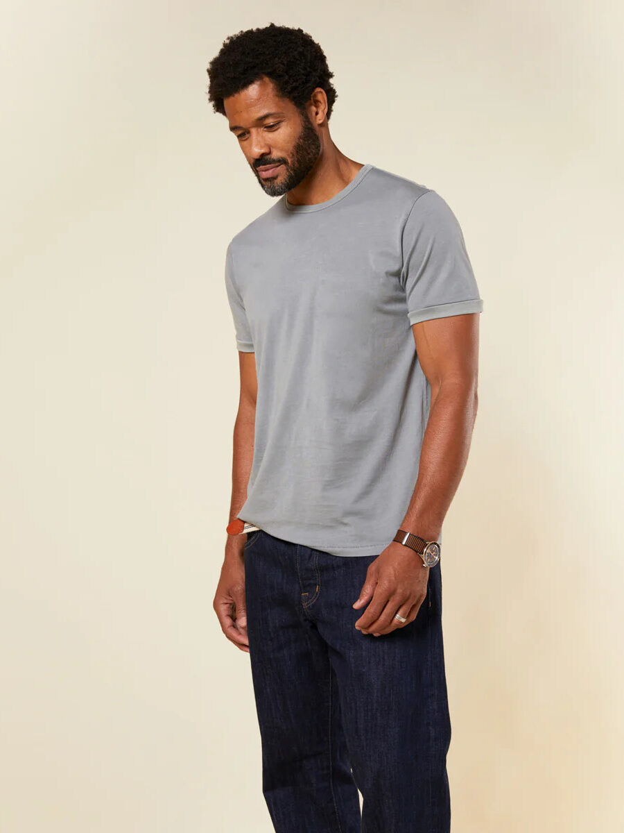 A man wearing a grey t - shirt and blue jeans.