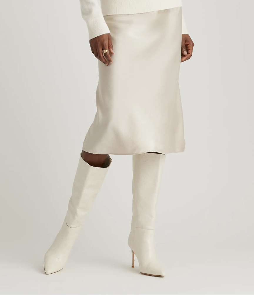Person wearing a white skirt and white knee-high boots walking against a neutral background.