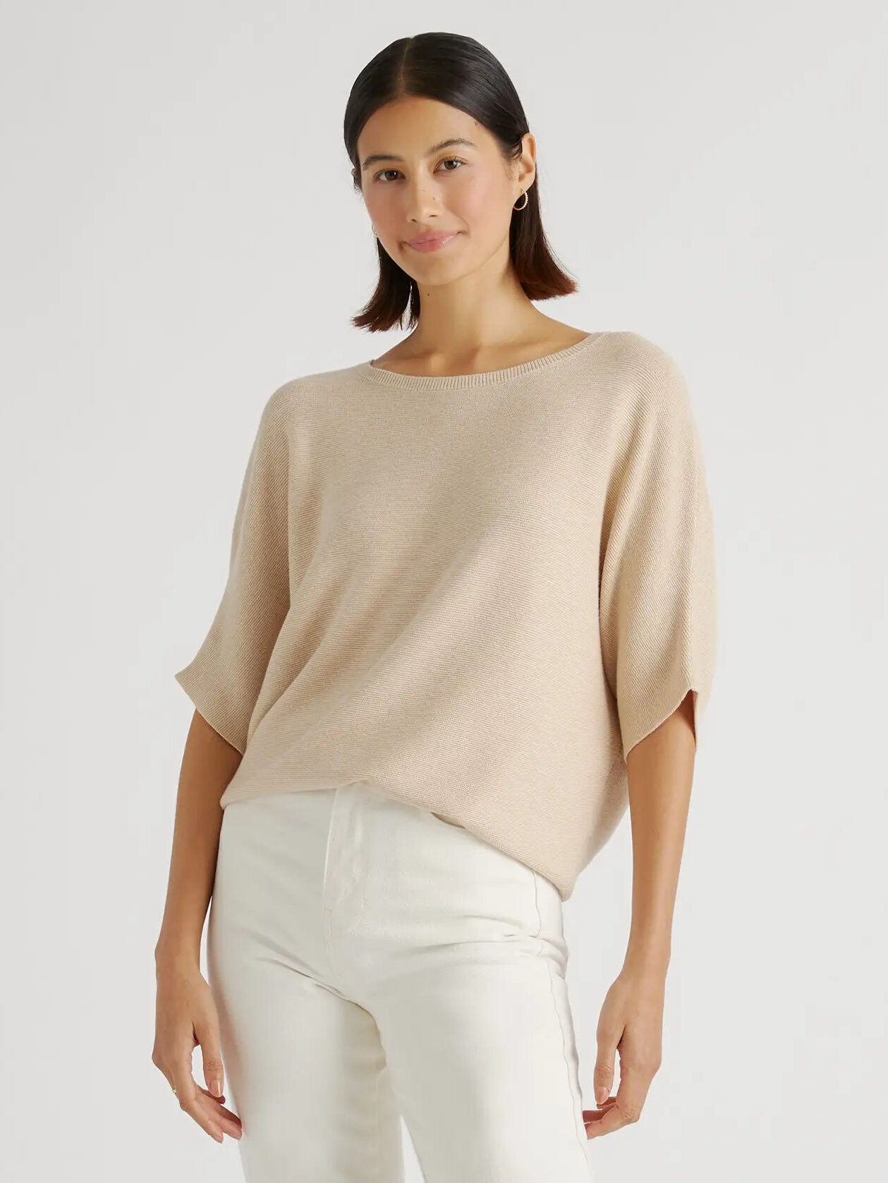 The model is wearing a beige sweater and white pants.