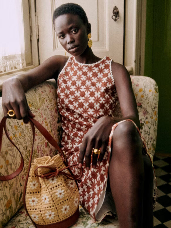 A woman sitting on a couch holding a straw purse.