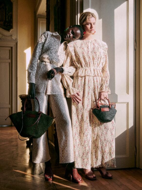 Two models posing in a vintage setting, wearing patterned dresses and holding handbags.