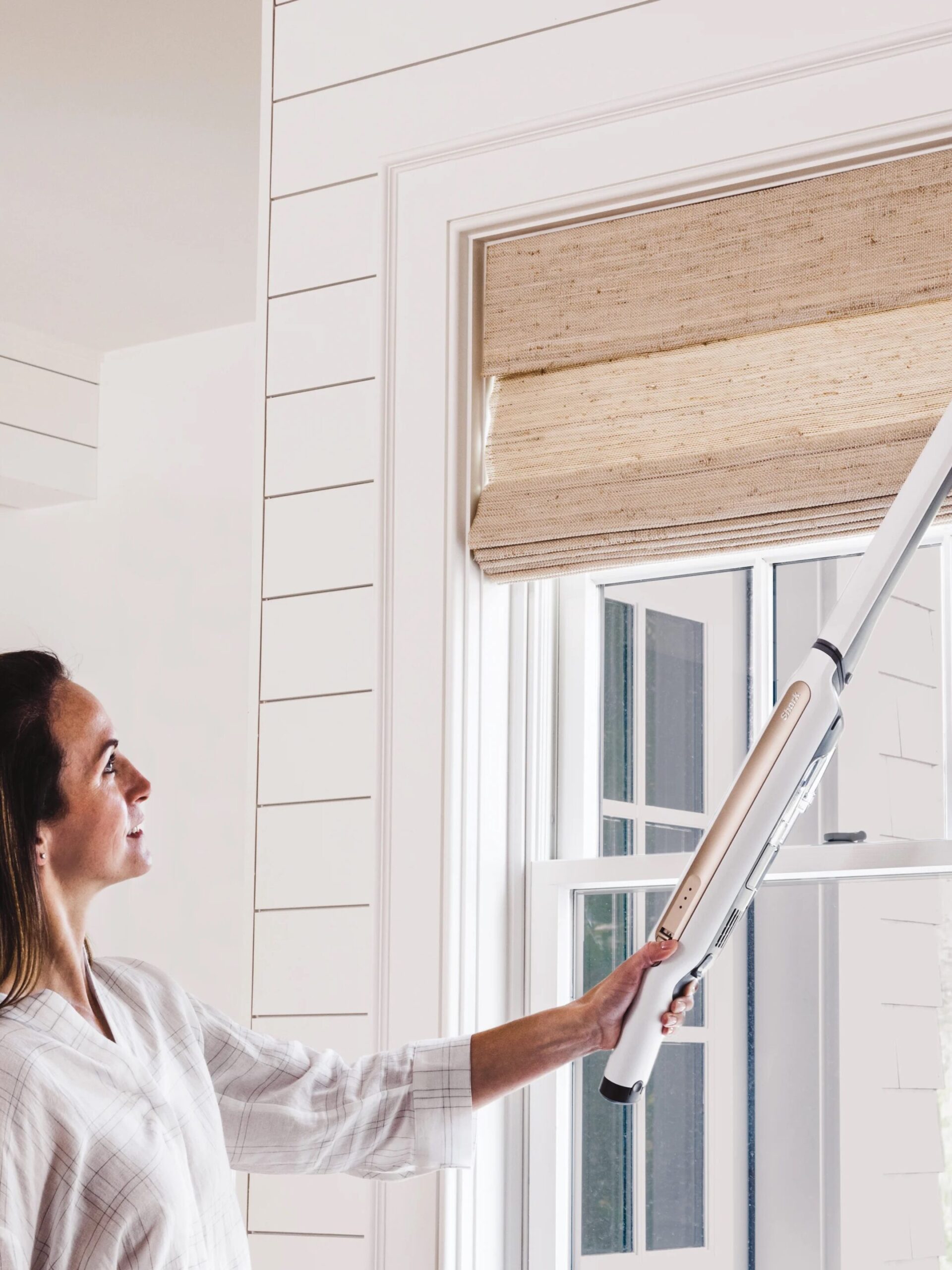 A model uses a Shark vacuum to clean their window blinds. 