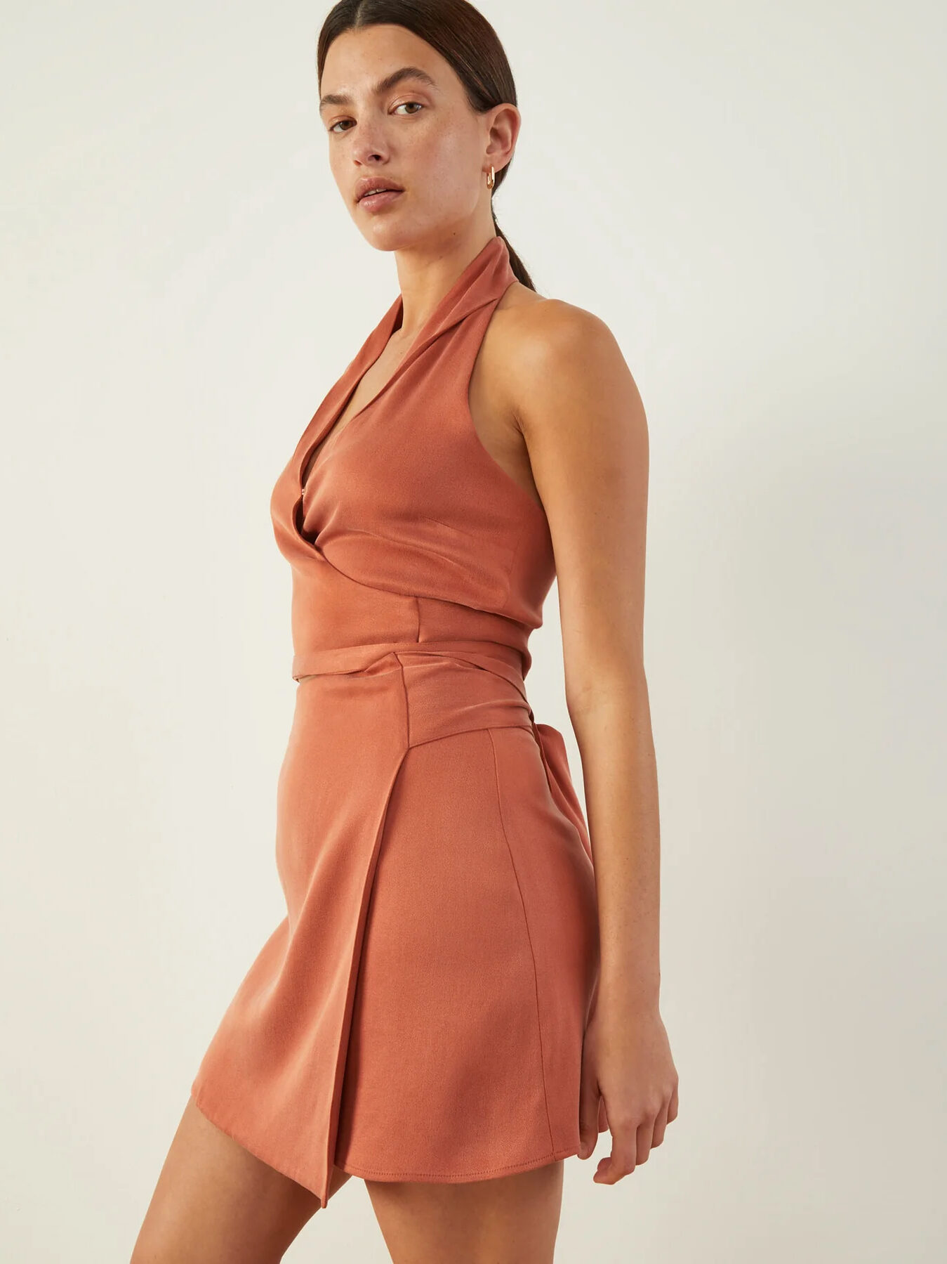 Woman posing in a sleeveless terracotta halterneck dress with a fitted waist.