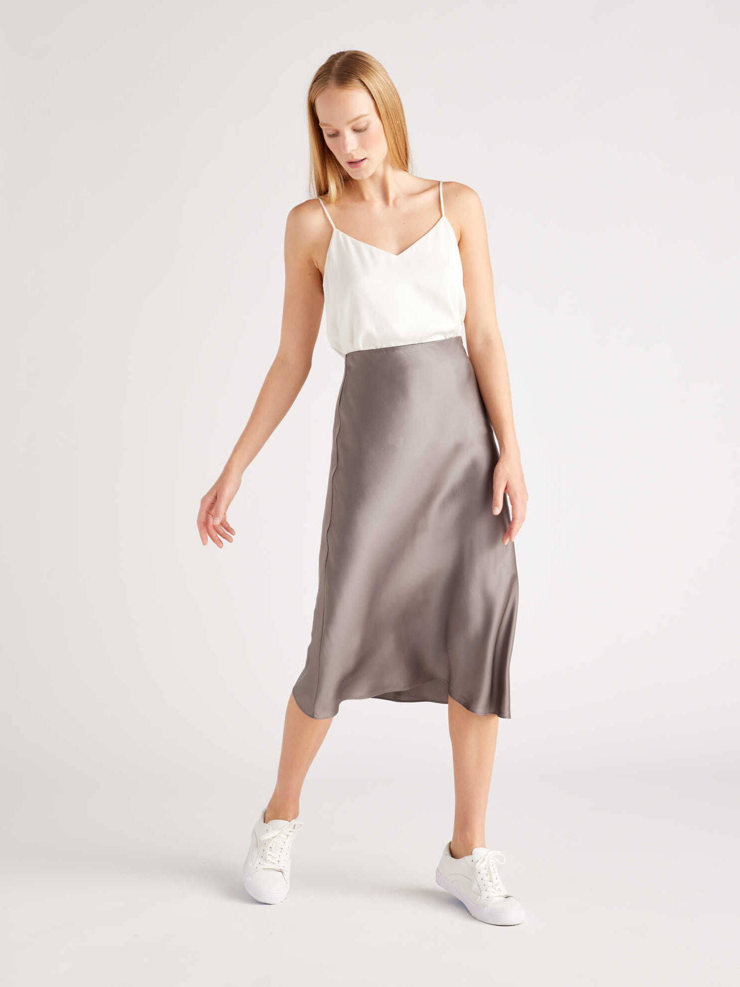 A woman modeling a white camisole top with a satin midi skirt and white sneakers.