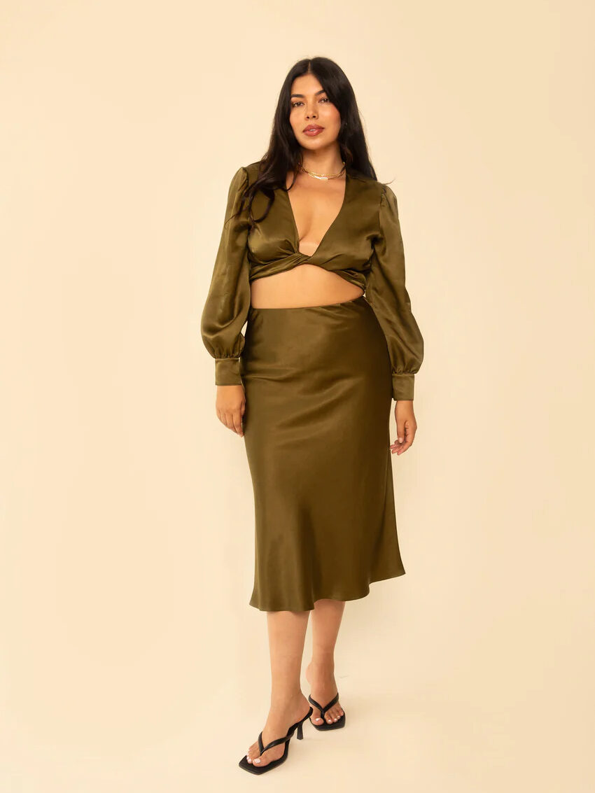 A woman wearing a green satin crop top with matching skirt and black heels.