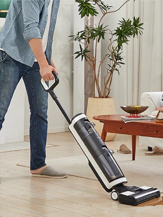 A person vacuuming the living room floor while a child and dog play nearby.