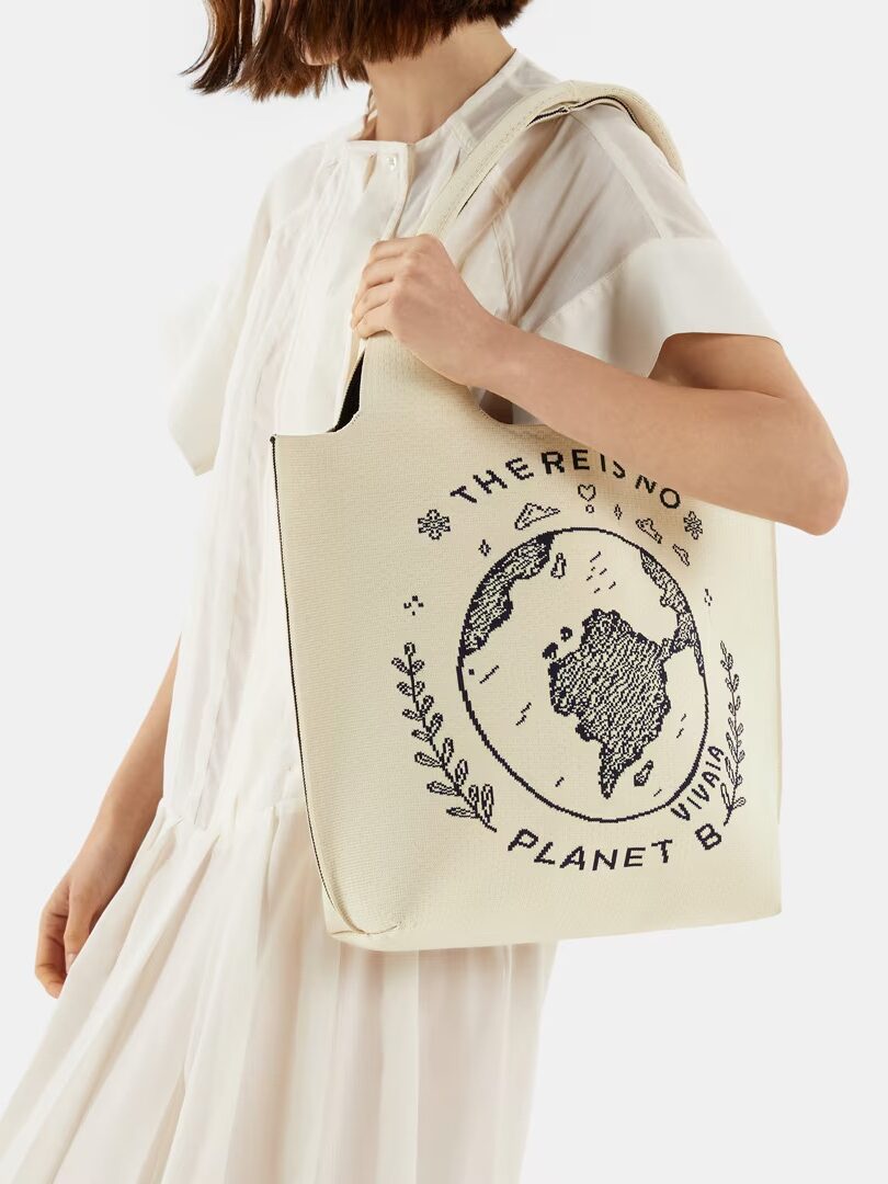 A person in a white outfit carrying a beige tote bag with an environmental message printed on it.