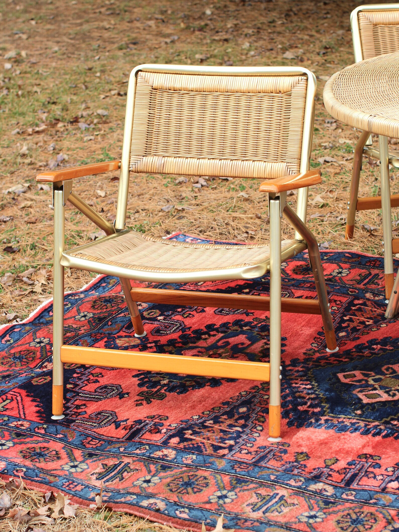 A table and chairs on a rug in the woods.