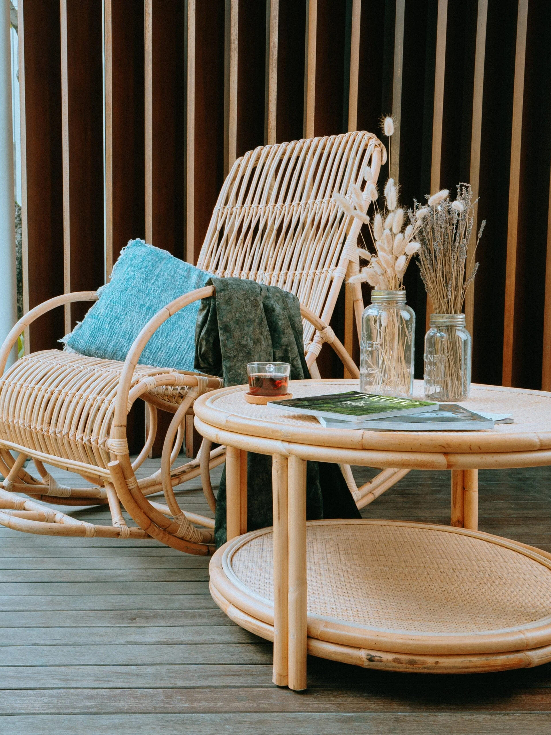 A rattan rocking chair and table on a wooden deck.