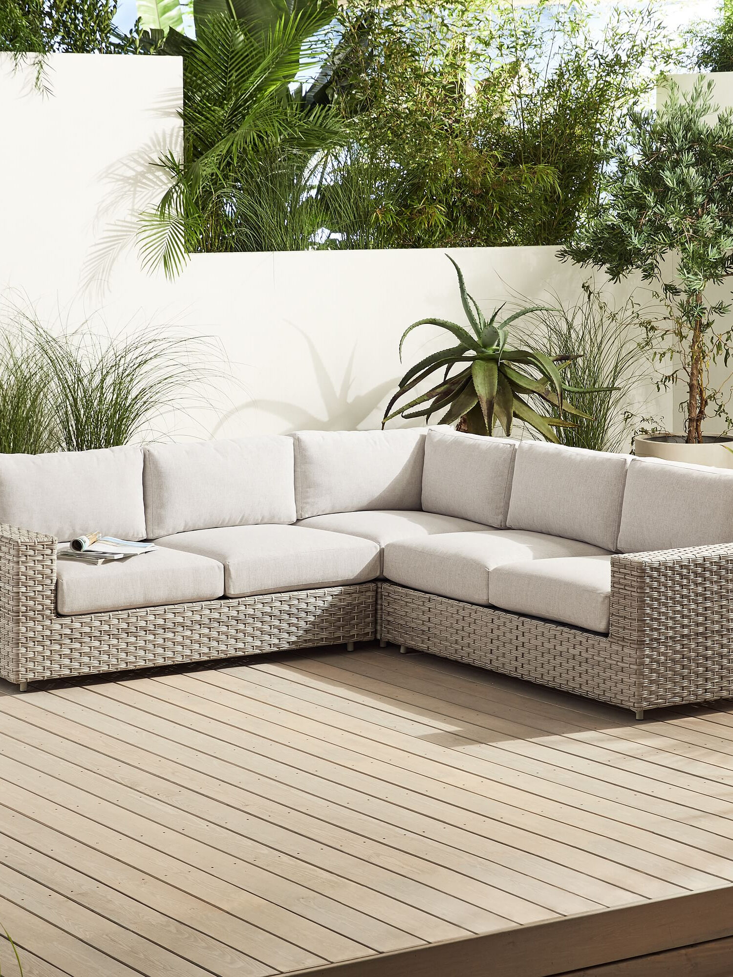 A white wicker sectional sofa on a wooden deck.
