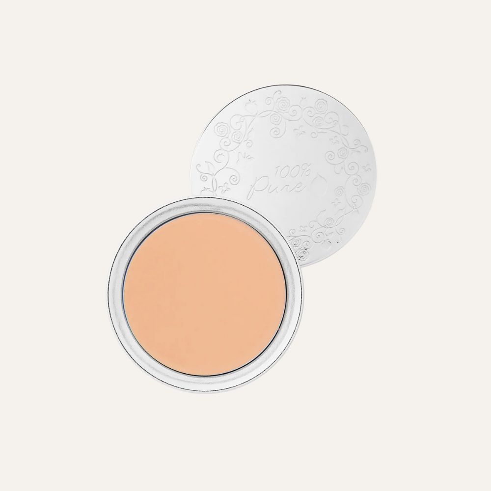 A compact foundation in an open silver case with a floral pattern on the lid, showing an orange-tinted pressed powder.