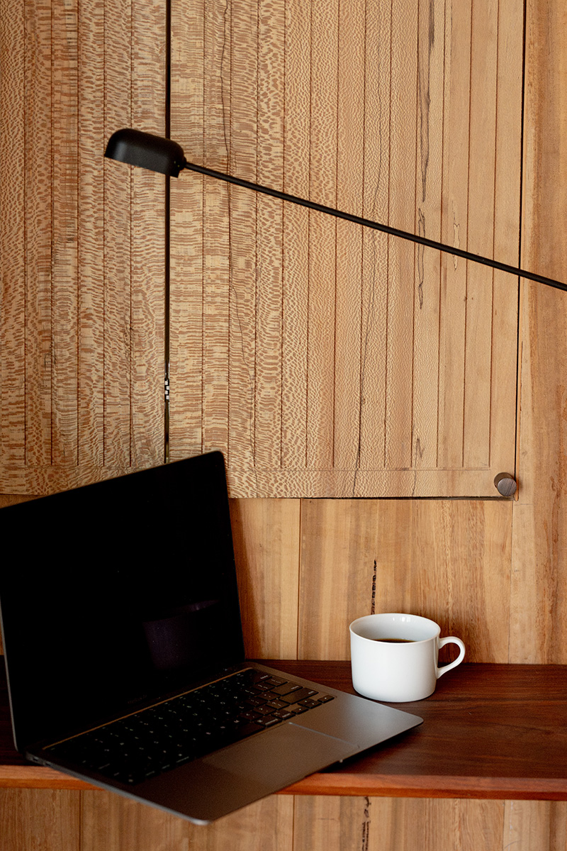 A laptop with a black screen and a white coffee mug on a wooden desk, positioned against a wooden background with a pull-down cane visible.