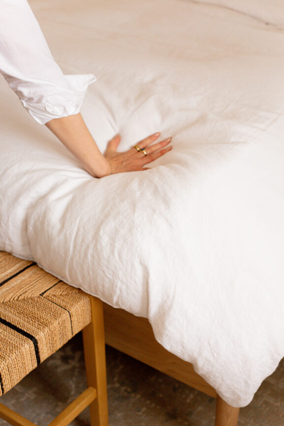 A person in a white shirt pressing their hand onto a fluffy white pillow on a wooden bench.