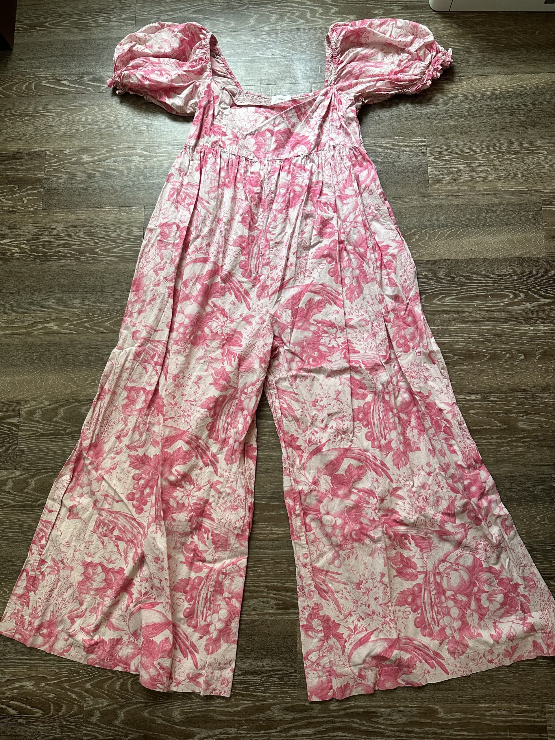 A pink floral jumpsuit with puffed sleeves spread out on a wooden floor.