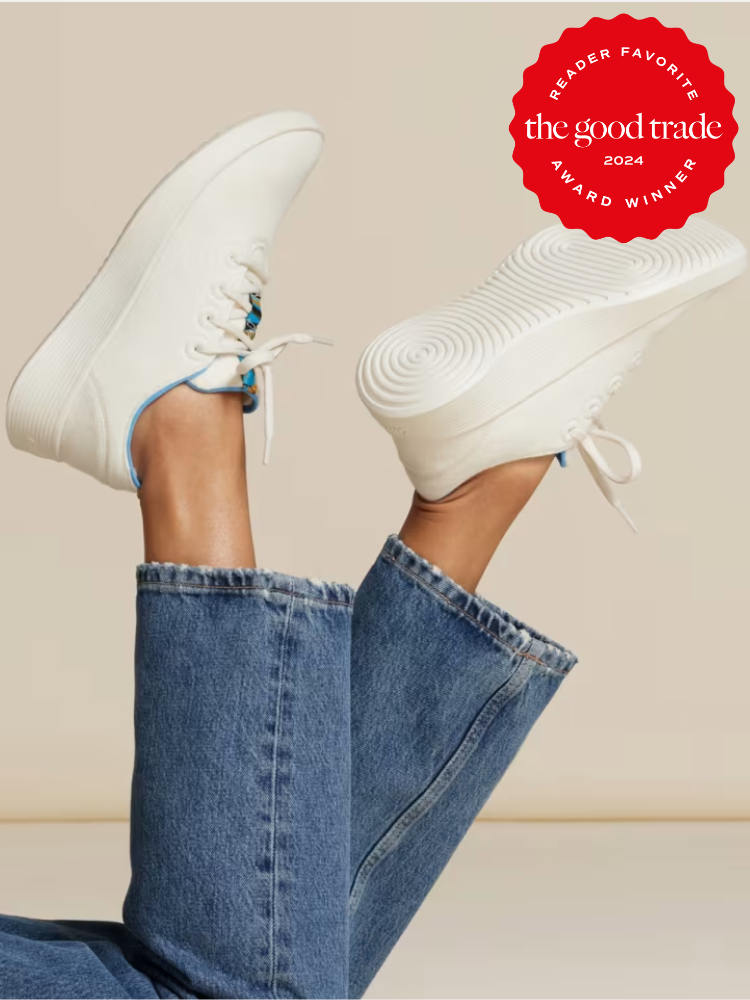 A pair of legs clad in blue jeans, one foot raised to show the sole of a white sneaker labeled as "the good trade award winner 2024.