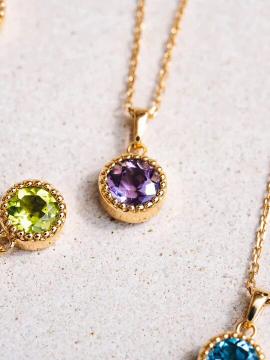 Gold pendants with various colored gemstones on a neutral background.