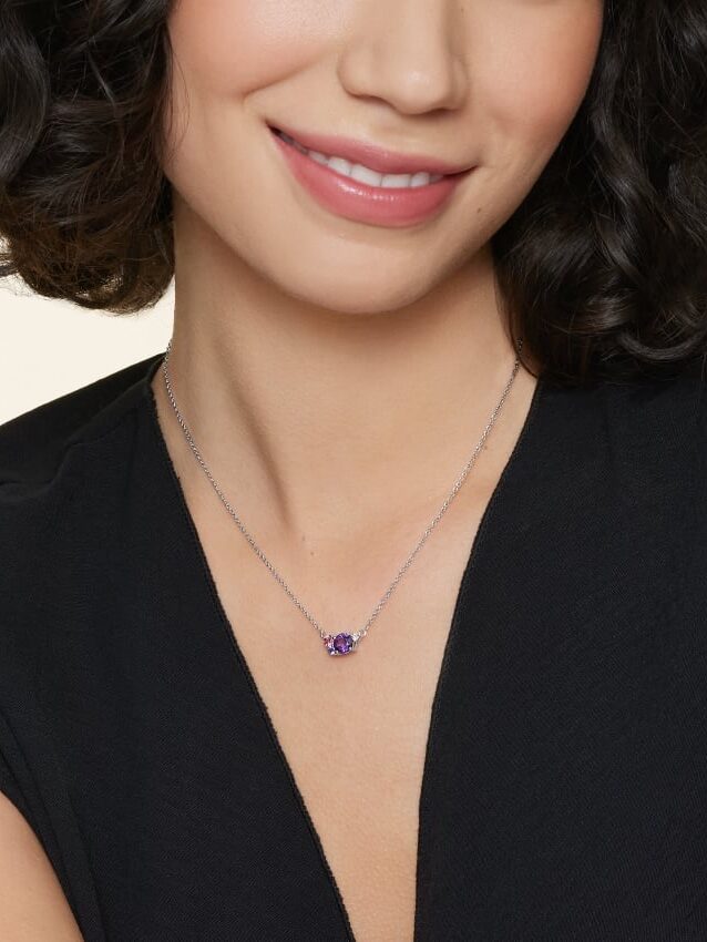 Woman smiling wearing a black top and a purple pendant necklace.