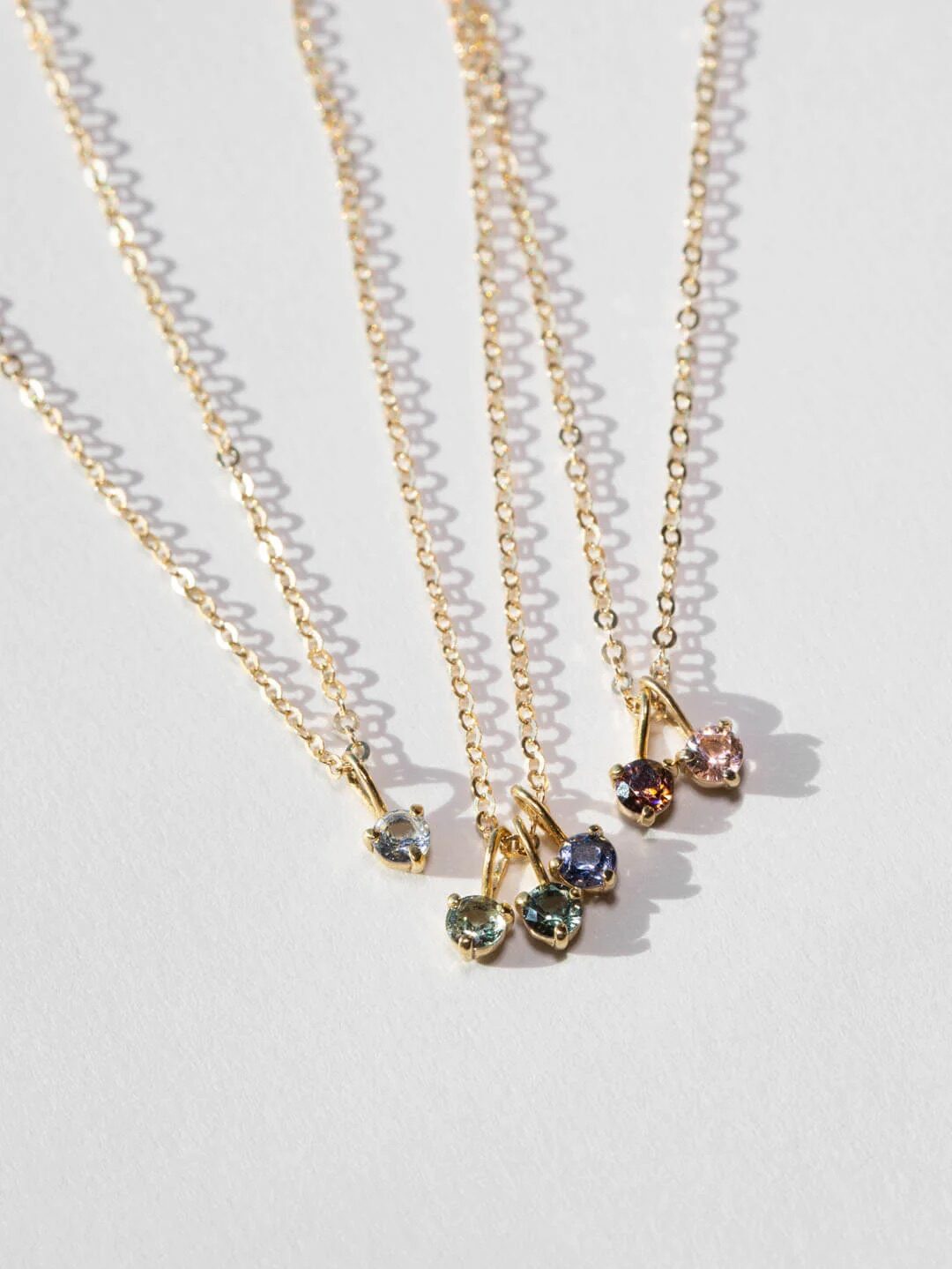 Five delicate gold necklaces with various colored gemstone pendants on a white surface.
