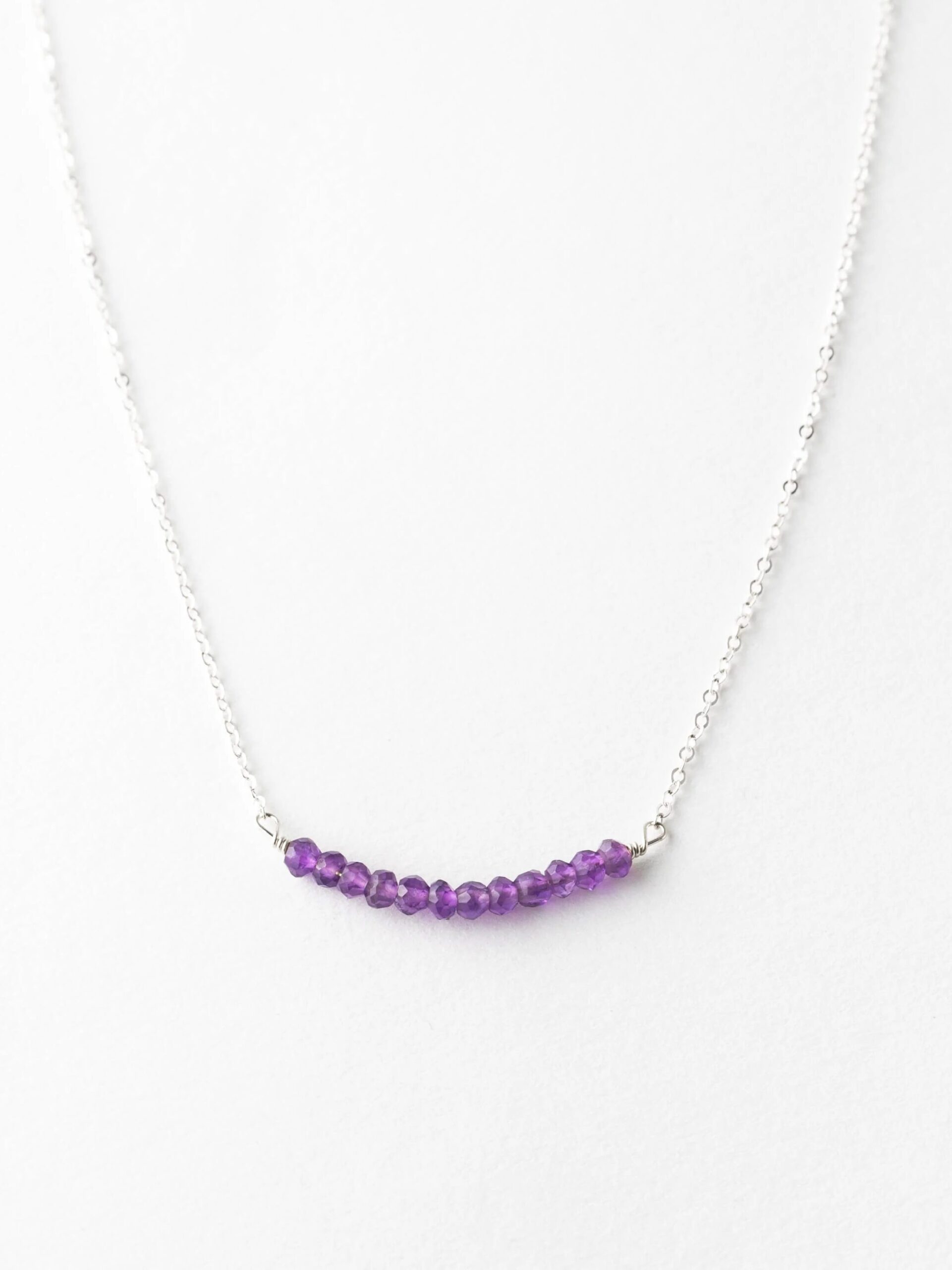Silver necklace with a curved row of purple beads against a white background.