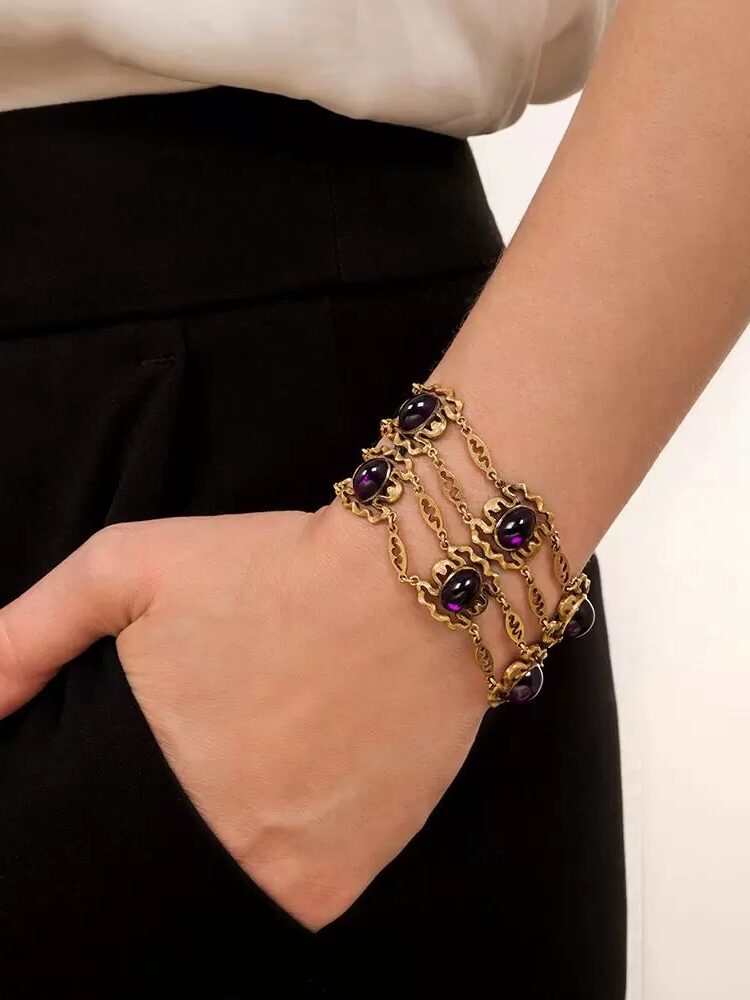 A person wearing a bracelet with purple gemstones draped over their hand.