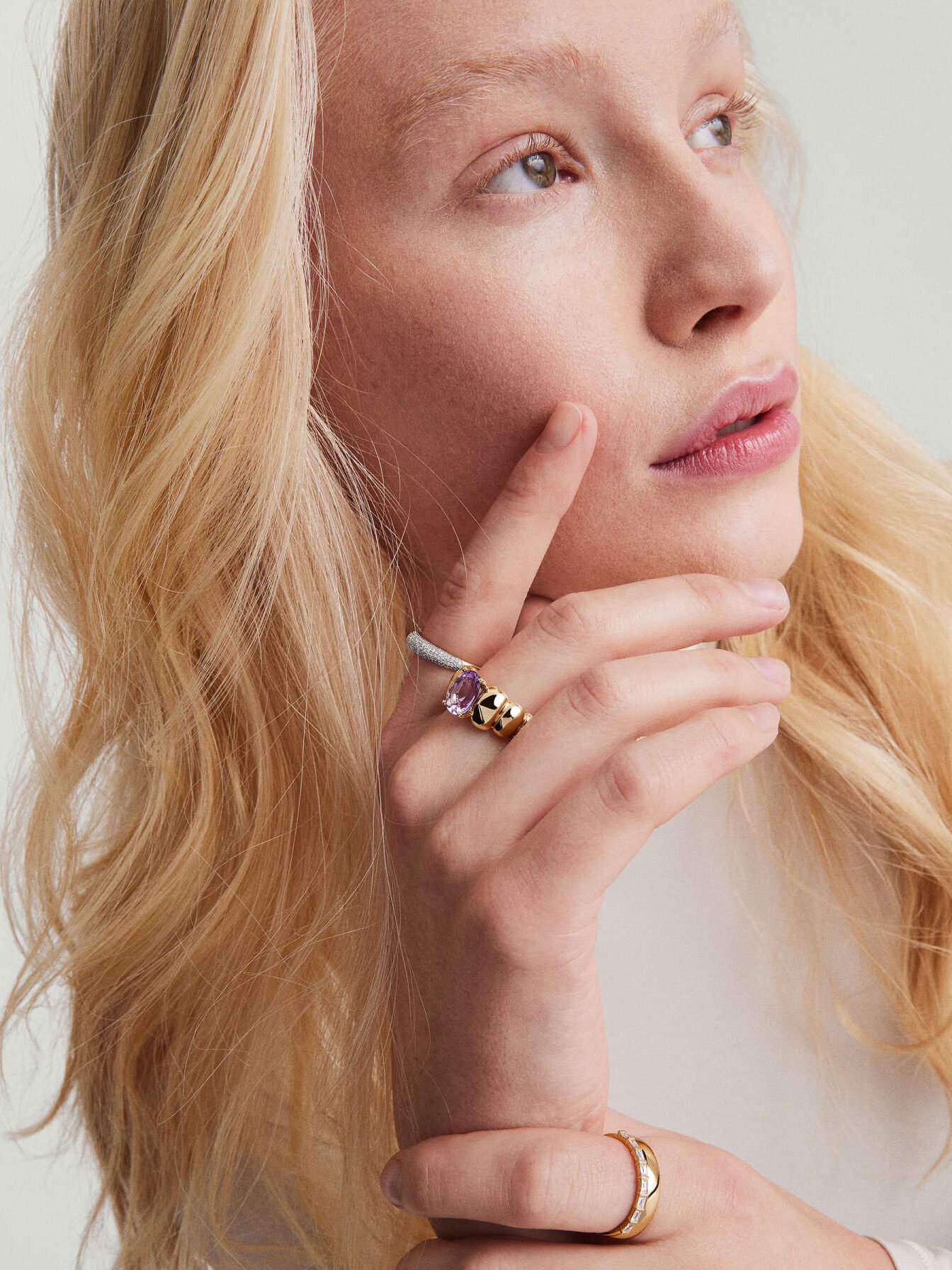 A woman with blonde hair showcasing a purple gemstone ring.
