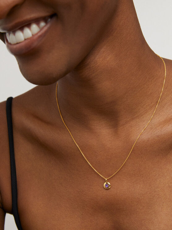 Smiling person wearing a delicate gold necklace with a single gemstone pendant.