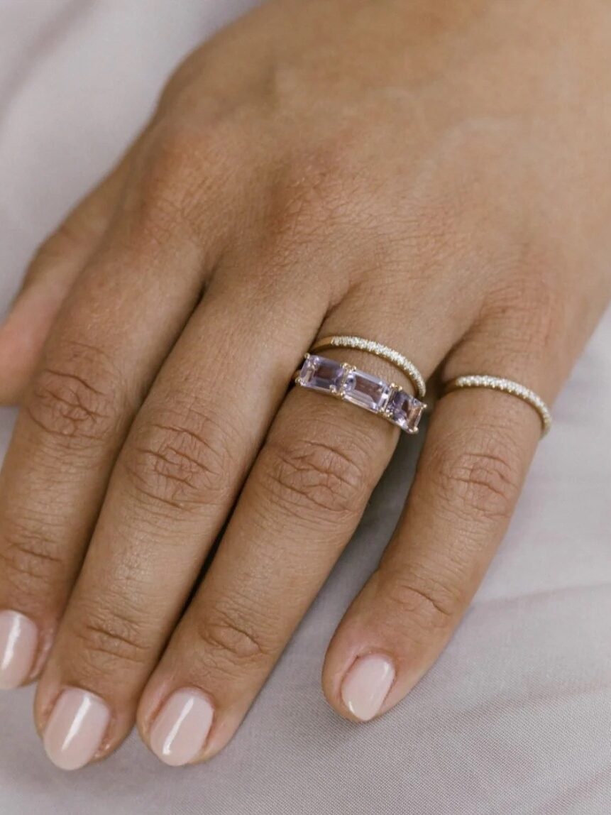 A hand adorned with two elegant rings, featuring a purple gemstone on the middle finger and a simple band on the fourth finger.