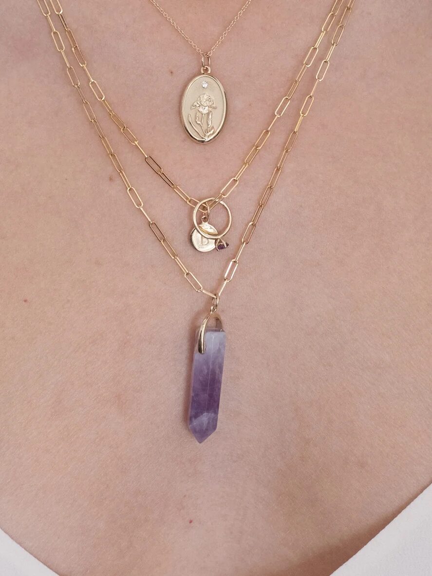 A person wearing a layered necklace set with a pendant and a crystal.