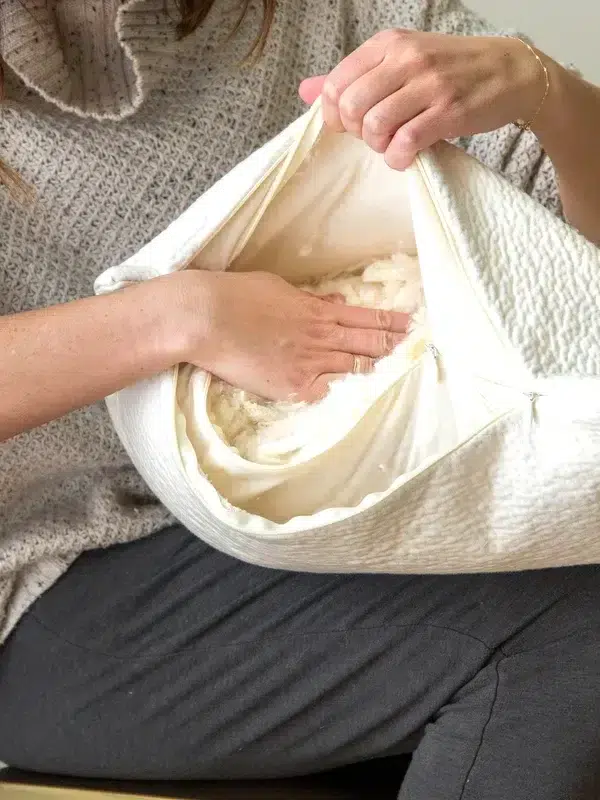 A person hand stuffing filling into a white fabric cushion.