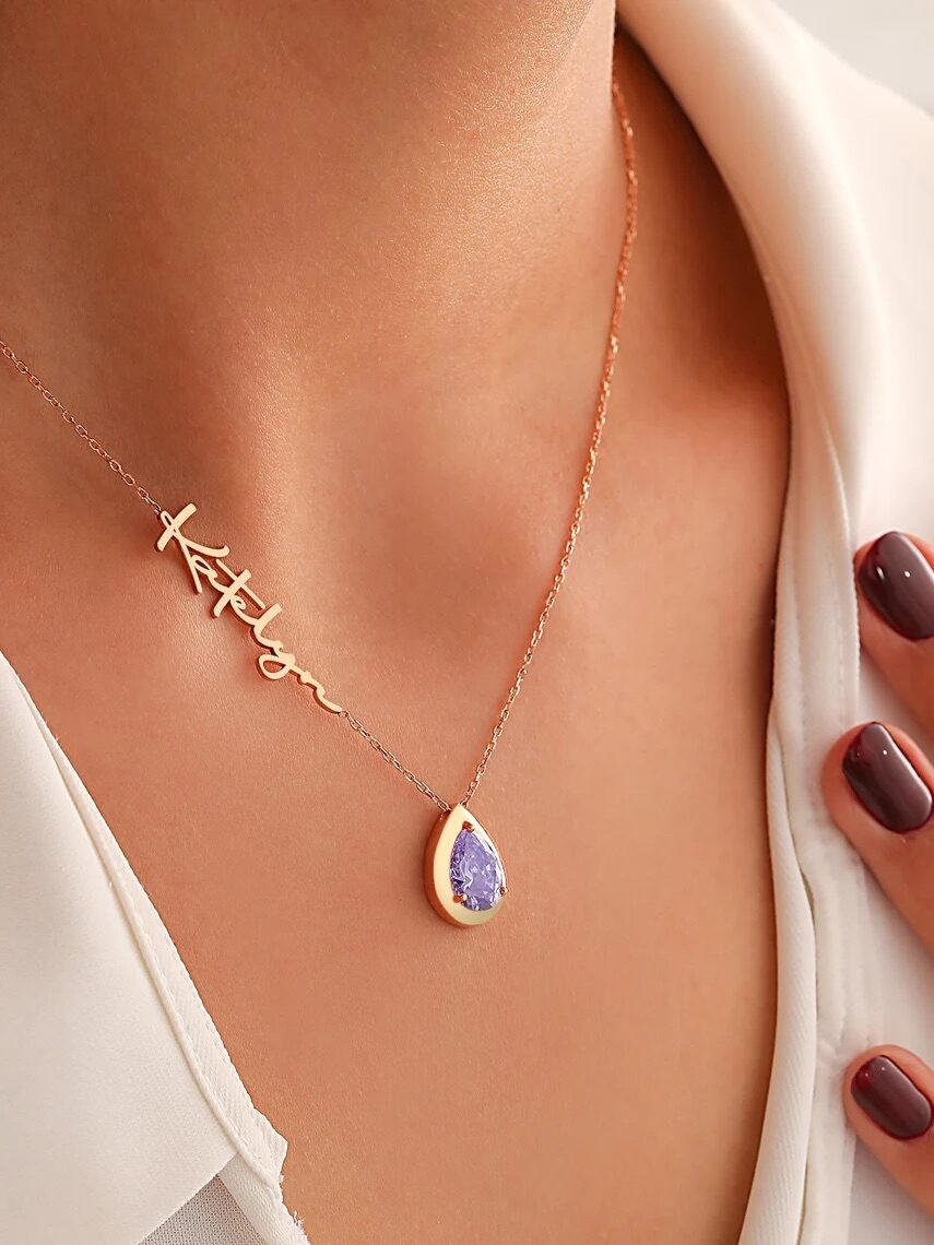 Close-up of a woman wearing a pendant and a cross necklace with the word "believe" scripted on it, showcasing manicured hands and a white blouse.