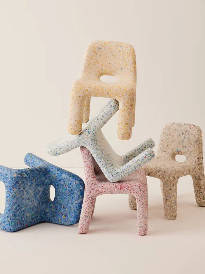 Five colorful terrazzo-style chairs stacked in an uneven, playful arrangement against a neutral background.