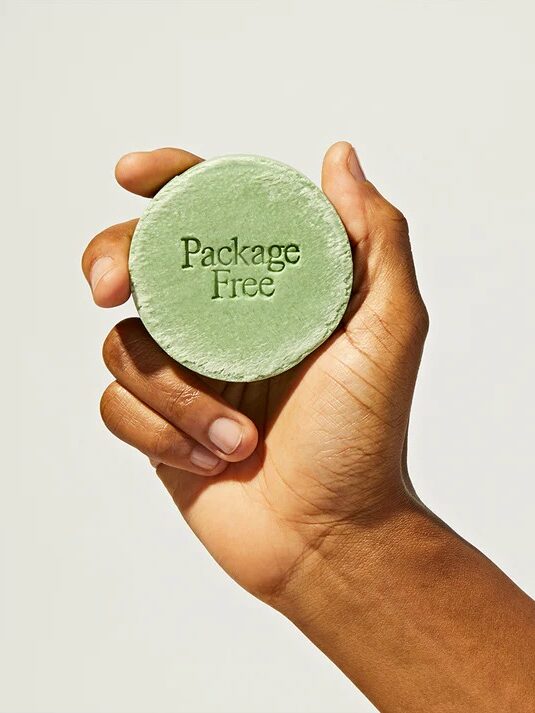 A hand holding a green "package free" labeled bar against a neutral background.