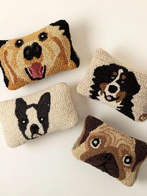 Four decorative pillows with knitted animal faces on a light background, featuring a variety of dog breeds.