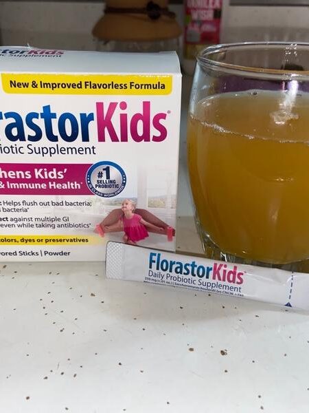 A box of florastorkids probiotic supplement with a packet in front and a glass of orange liquid, presumably mixed with the supplement, on a kitchen counter.