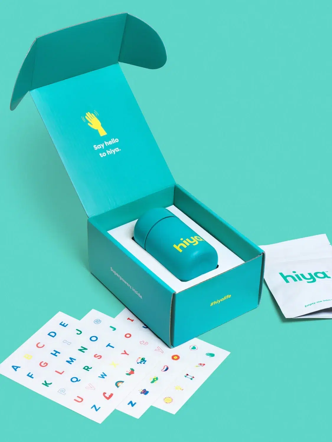 A children's vitamin product presented with its packaging, informational booklet, and alphabet stickers on a teal background.