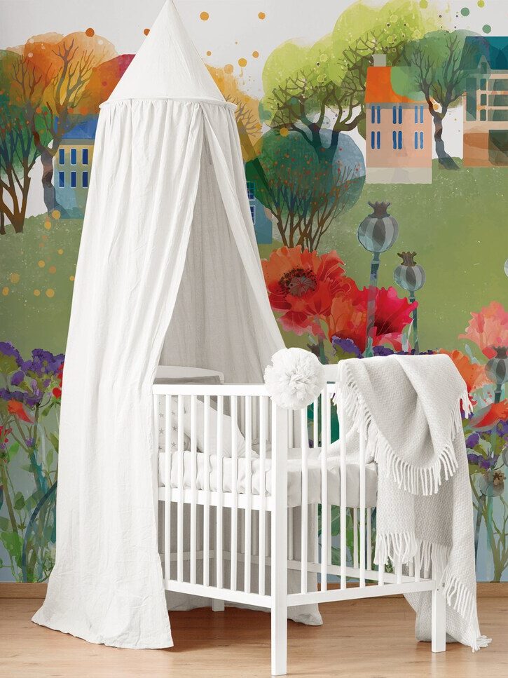 A nursery with a white crib, a draped canopy, and a colorful mural of a village and flowers on the wall.
