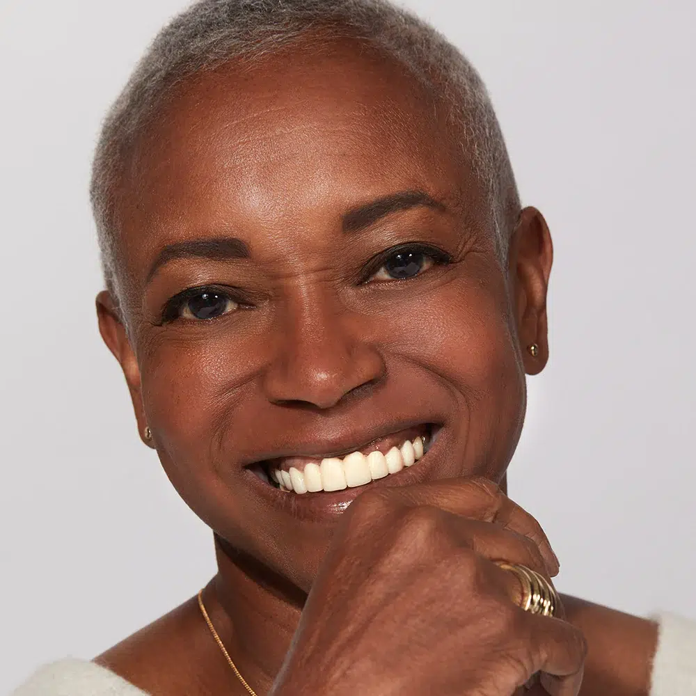 Portrait of a smiling elderly woman with short gray hair, wearing a white outfit, looking directly at the camera.