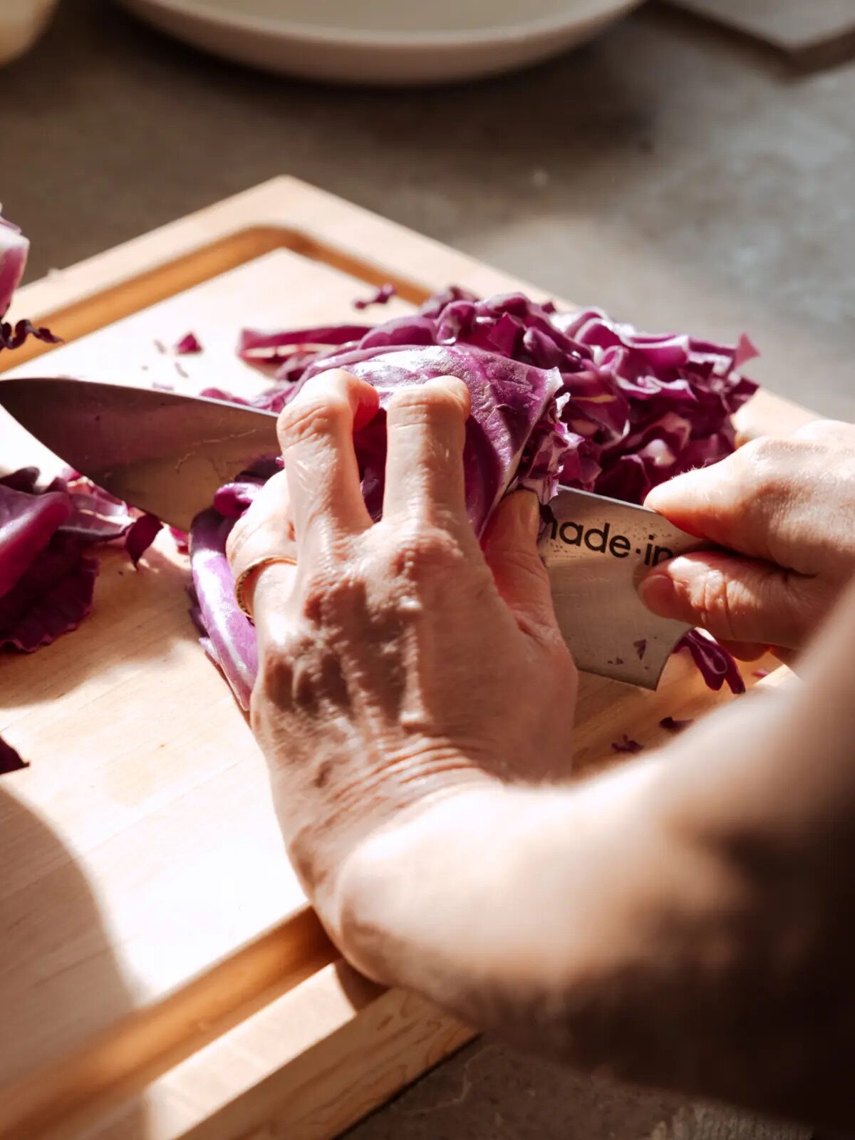 Hands slicing red cabbage on a wooden cutting board.