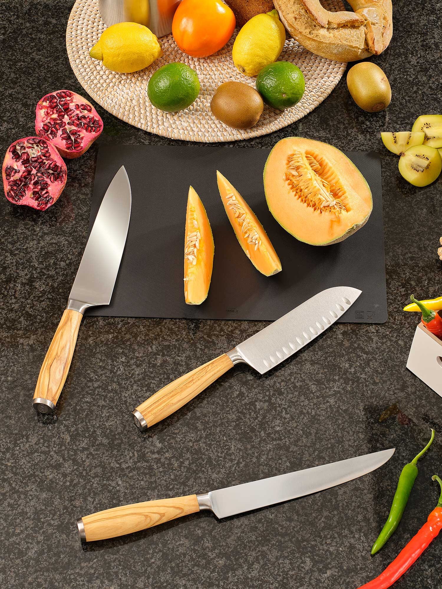 Kitchen counter with various fruits, vegetables, and a set of knives with wooden handles.