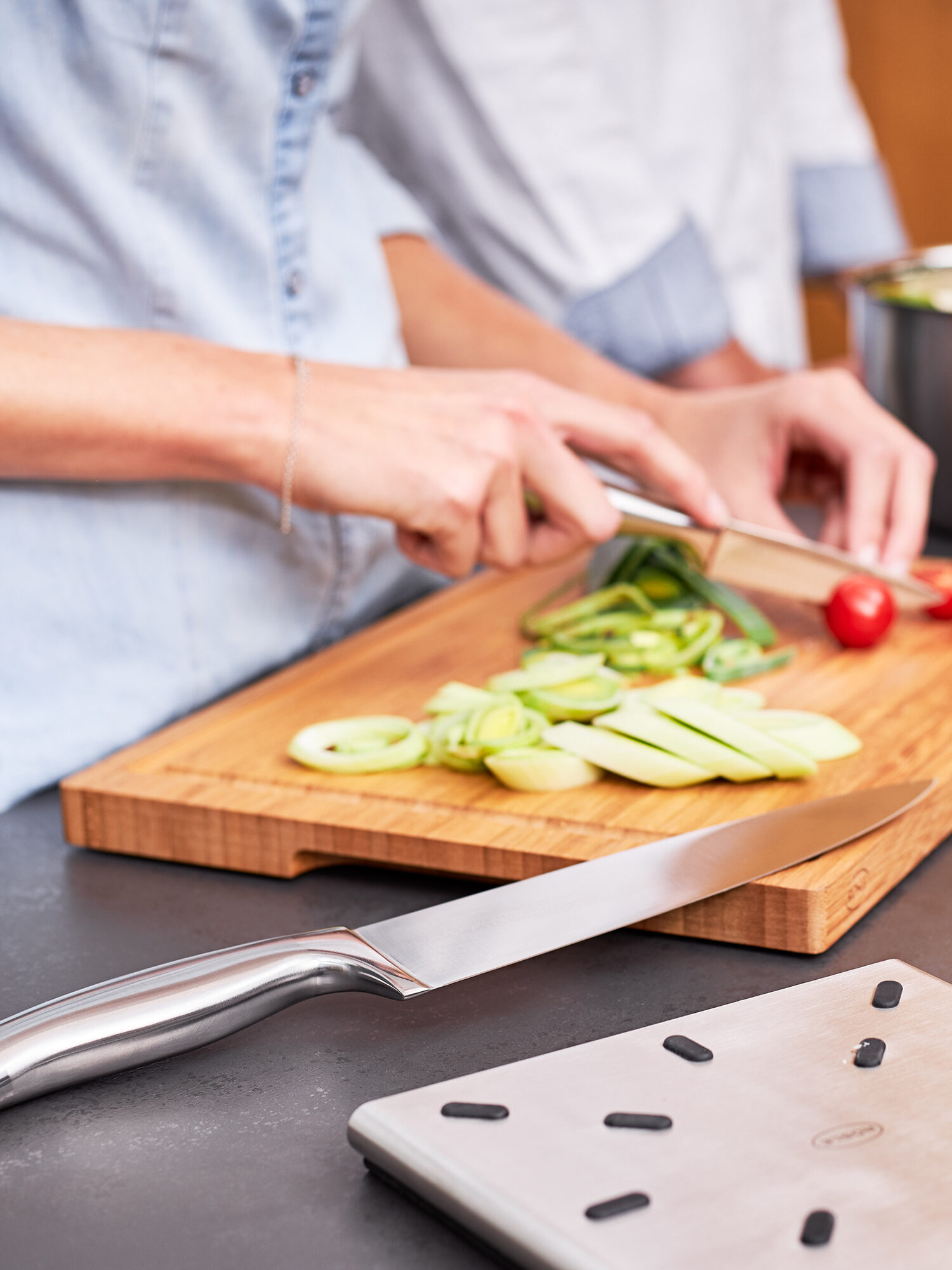 A person slicing cucumbers and tomatoes on a wooden cutting board in a kitchen, with a focus on their hands and the vegetables.